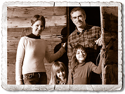 Persia family: mom, dad and two daughters standing in front of rustig building. Black and white photograph, sepia-toned